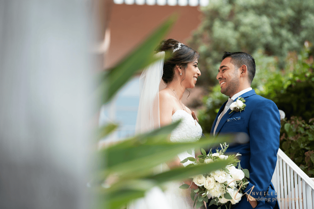 Intimate portrait of bride and groom smiling framed by leaves: Wedding photography shots.