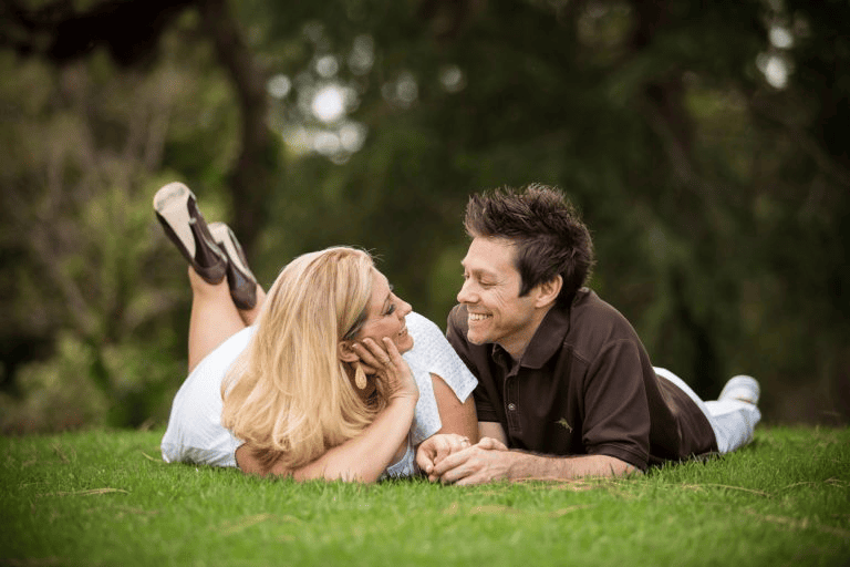 Couple lying on grass looking into each other's eyes for Engagement Photo Ideas.