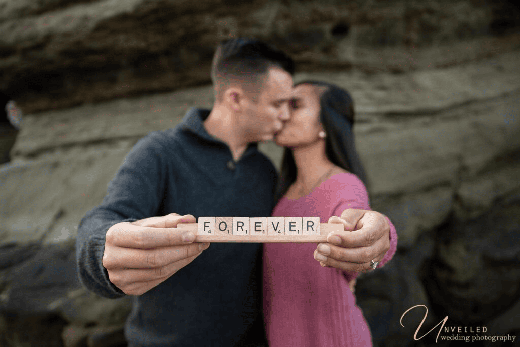 Couple holding FOREVER tile sign while kissing for romantic Engagement Photo Ideas.