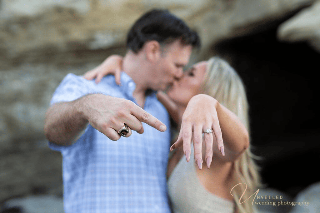 Close-up of diamond engagement ring with kissing couple for Engagement Photo Ideas.