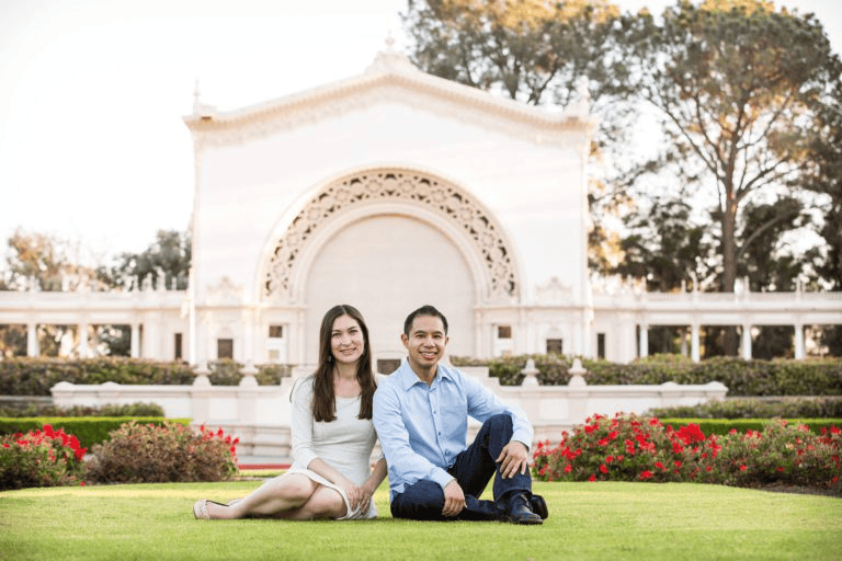 Couple sitting on lawn in front of ornate arch pavilion for Engagement Photo Ideas.