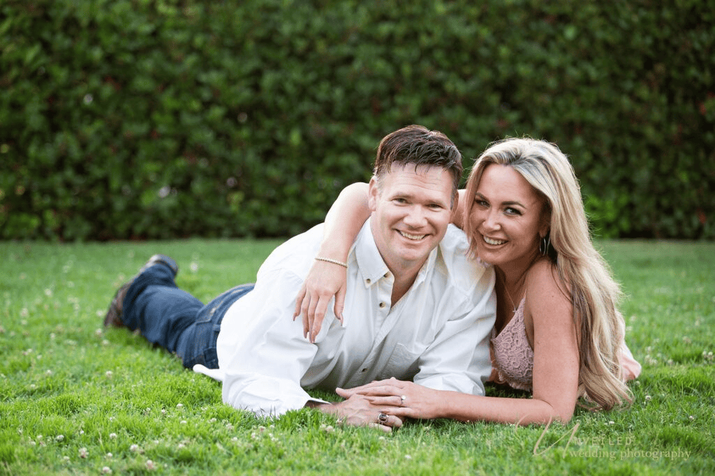 Happy couple lying on green grass smiling for relaxed outdoor Engagement Photo Ideas.