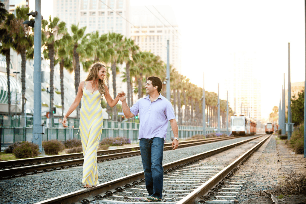 Couple walking along train tracks framed by palm trees for Engagement Photo Ideas.