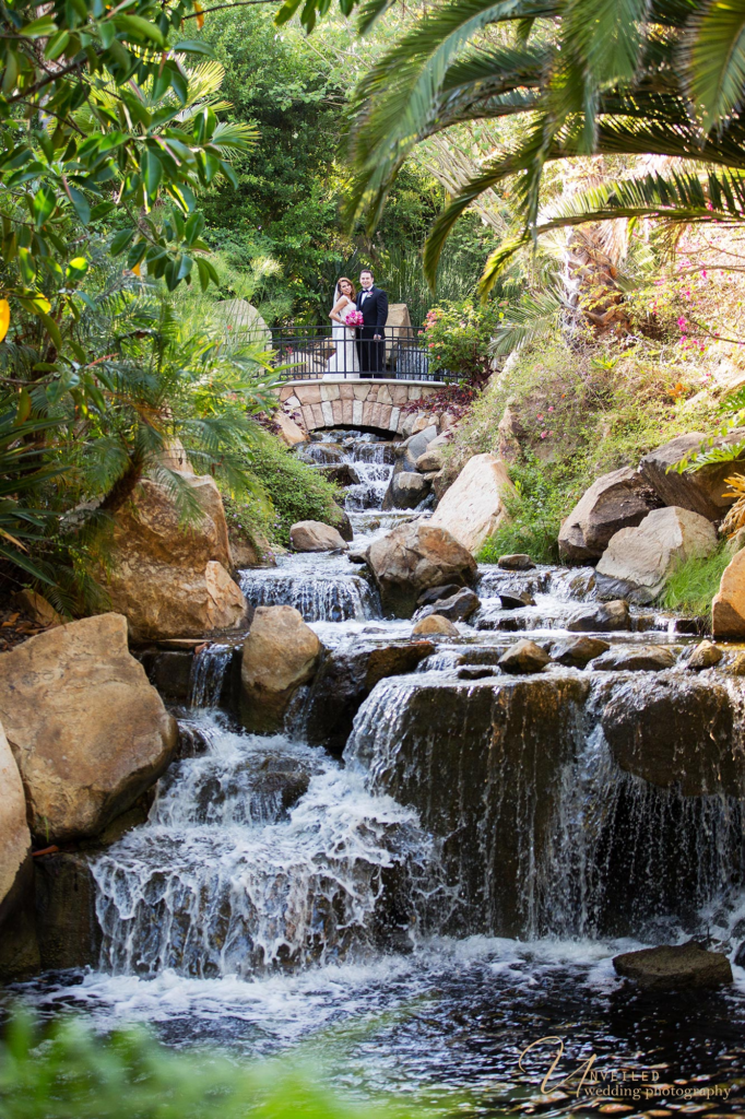 Couple standing on bridge above waterfall by Grand Tradition Estate Wedding Photographer.