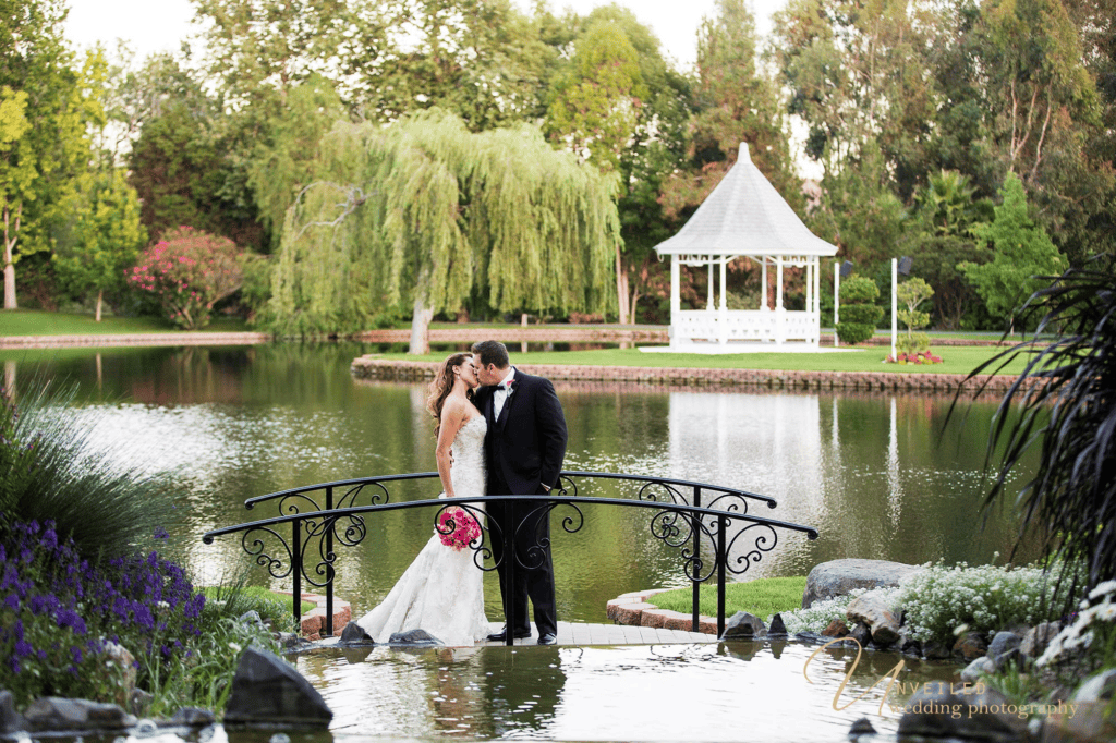 Couple kissing on bridge near lake gazebo by Grand Tradition Estate Wedding Photographer.