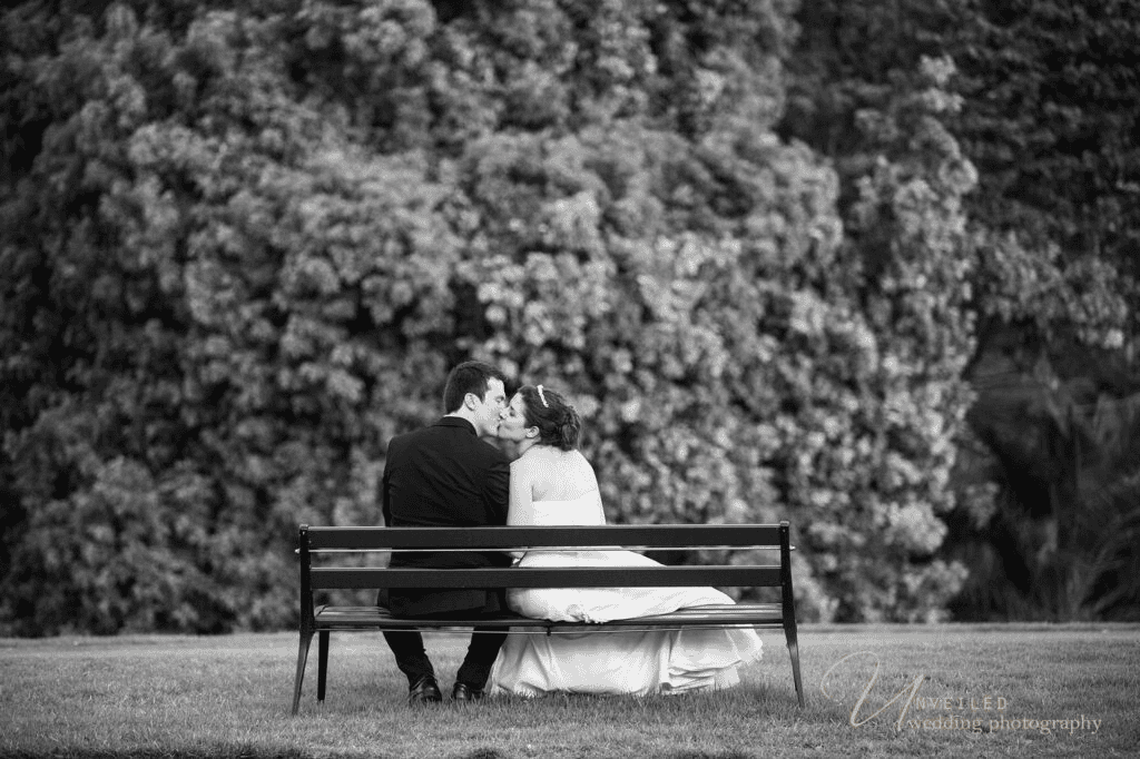 Black and white kissing couple on park bench in fine art vs documentary wedding photography.