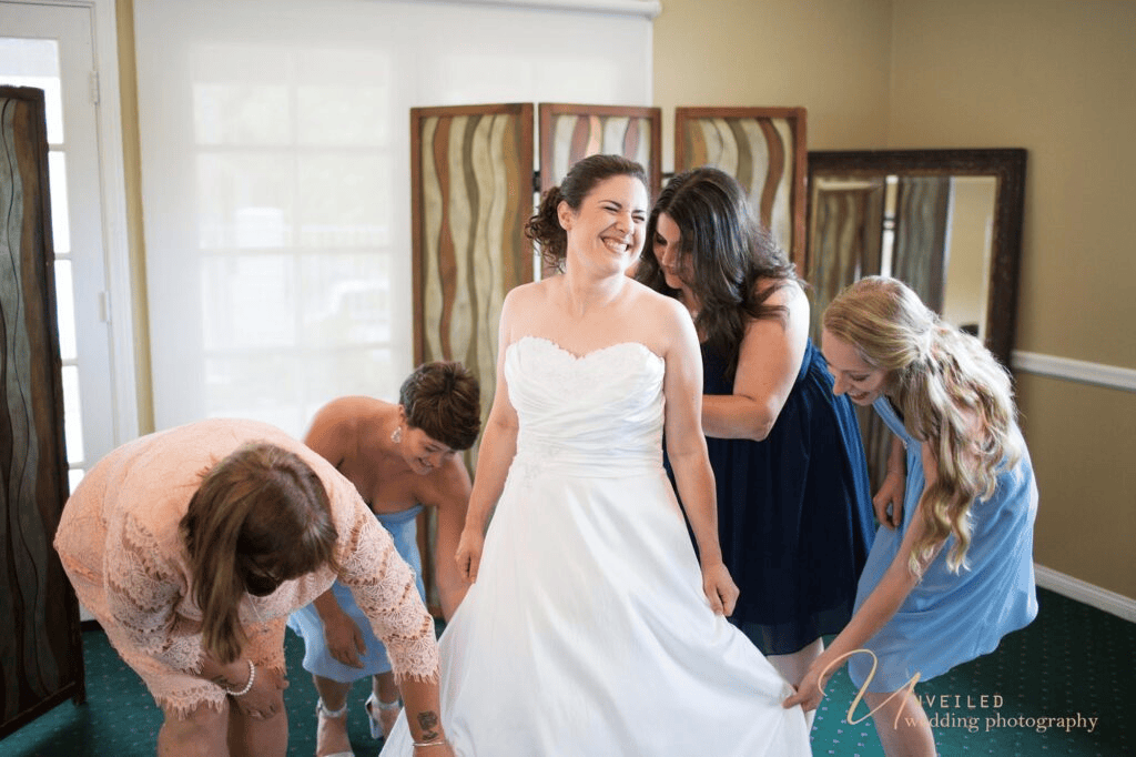 Bridesmaids helping laughing bride in candid fine art vs documentary wedding photography.
